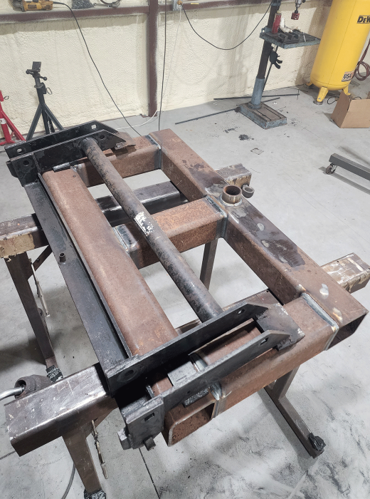 Fabricated steel frame assembly with square tubing and crossbars on a welding table.