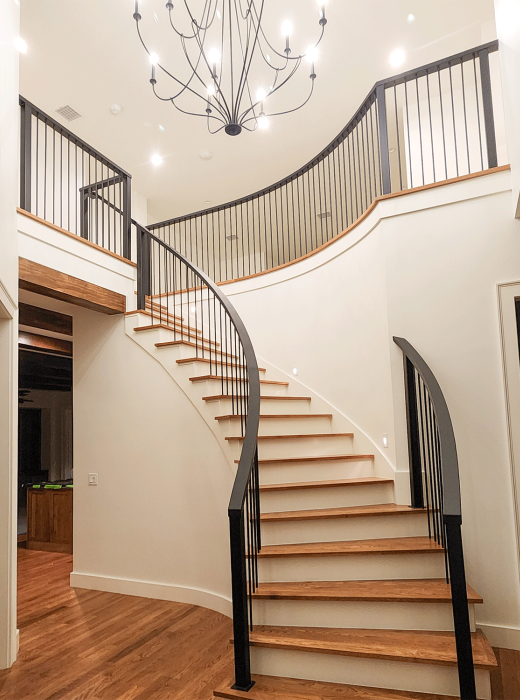 Curved wood staircase with custom black metal handrail and balusters in a modern foyer.
