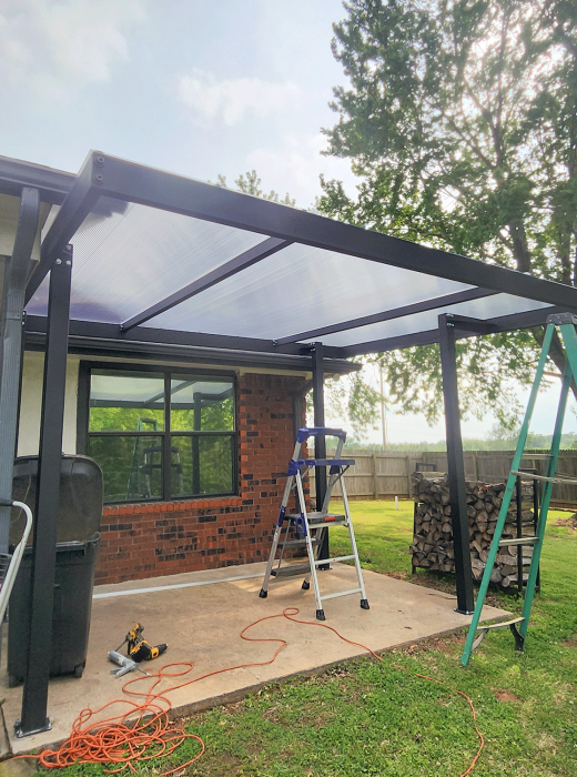 Back patio with custom black metal pergola frame and clear polycarbonate roof in progress.
