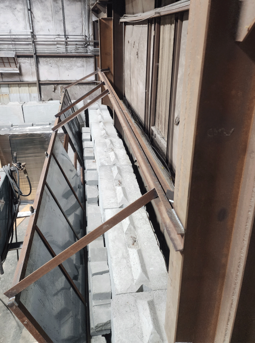 Industrial shop setup with long steel frames braced over stacked concrete blocks along a wall.