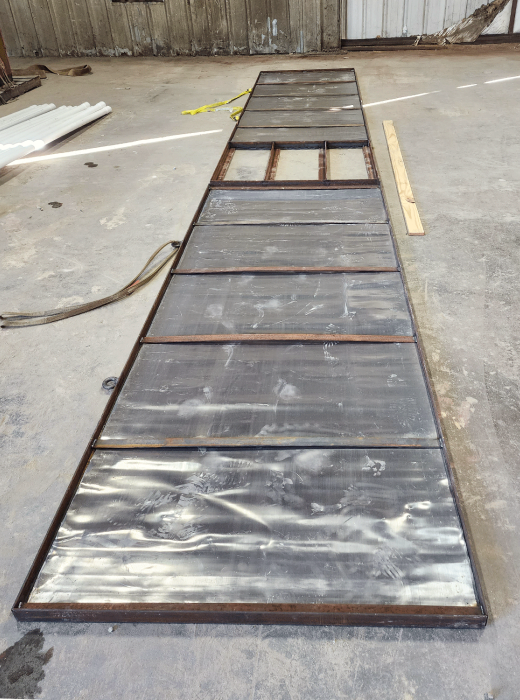 Large custom fabricated steel panel with segmented sections laid flat on a shop floor.