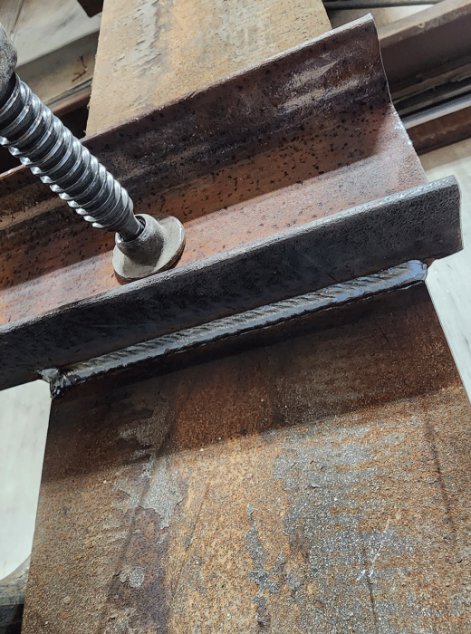 Close-up of a steel beam with a welded plate clamped in place for fabrication.