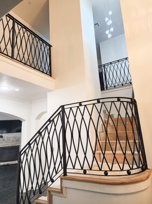 Custom black metal stair railing with woven wave pattern in a two-story foyer.