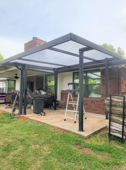Modern backyard patio with custom black steel canopy and clear roof attached to brick home.