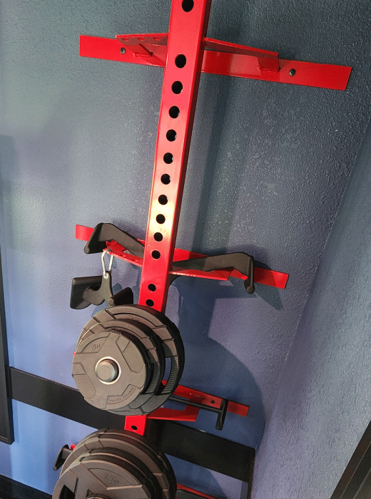 Red wall-mounted steel rack with round holes holding gym attachments and weight plates.