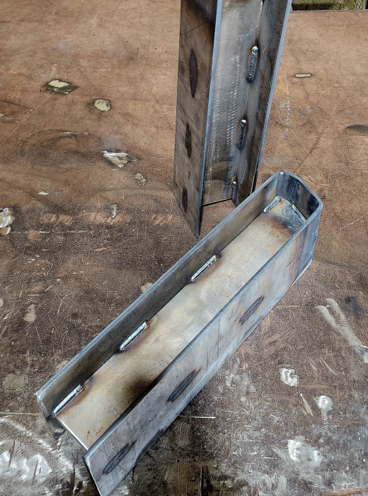 Fabricated steel channel sections with internal welds on a metal work table.