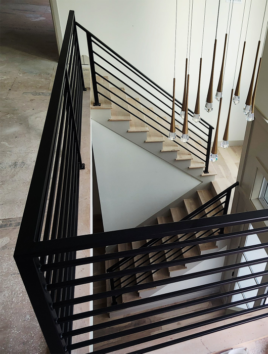 Modern interior staircase with black horizontal metal railing and light wood treads.