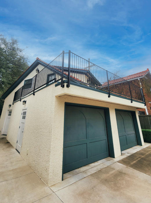 Two-car garage with upper patio enclosed by custom black metal railing.