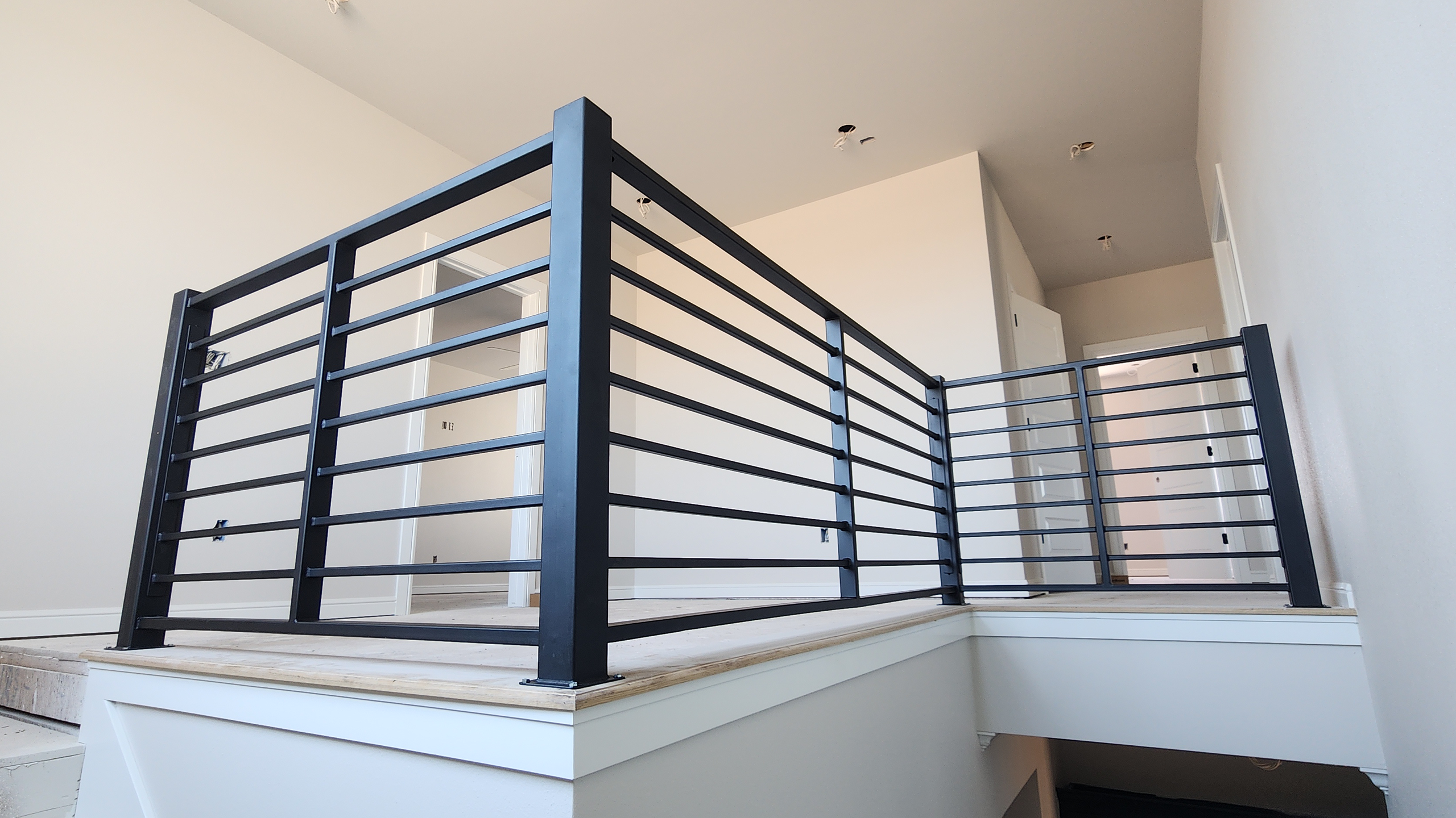 Modern upper landing with custom black horizontal metal guardrail in a new construction home.