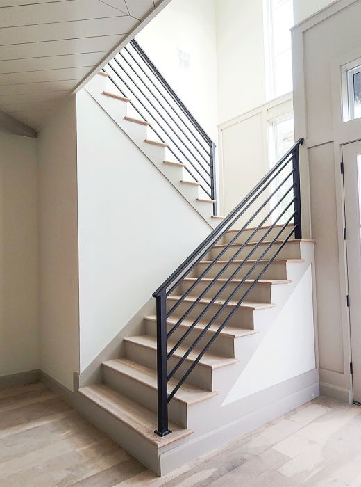Modern interior staircase with custom black metal railing and light wood treads in a bright entryway.