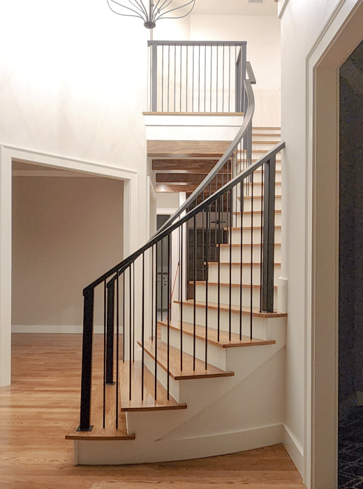 Curved wood staircase with custom black metal railing and vertical balusters in a modern foyer.