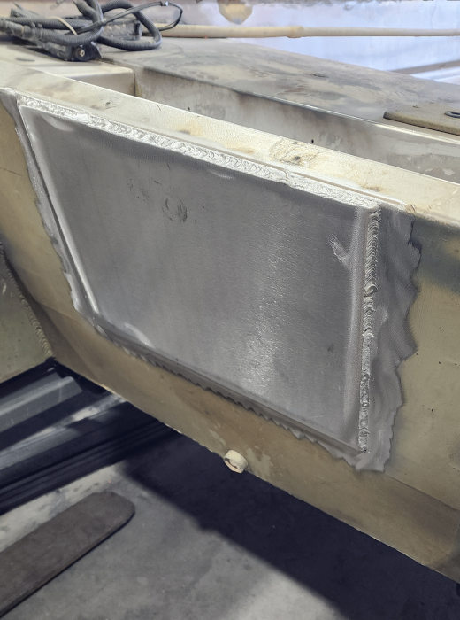 Aluminum patch panel fully welded into a larger metal surface during repair.