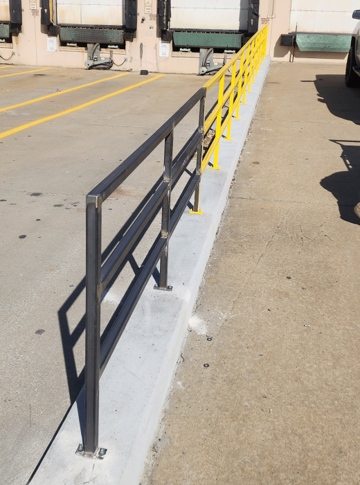 Steel safety railing system installed along a raised concrete curb at a loading dock.